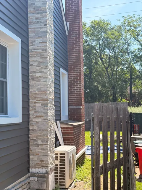 Finished stone veneer chimney beside house siding
